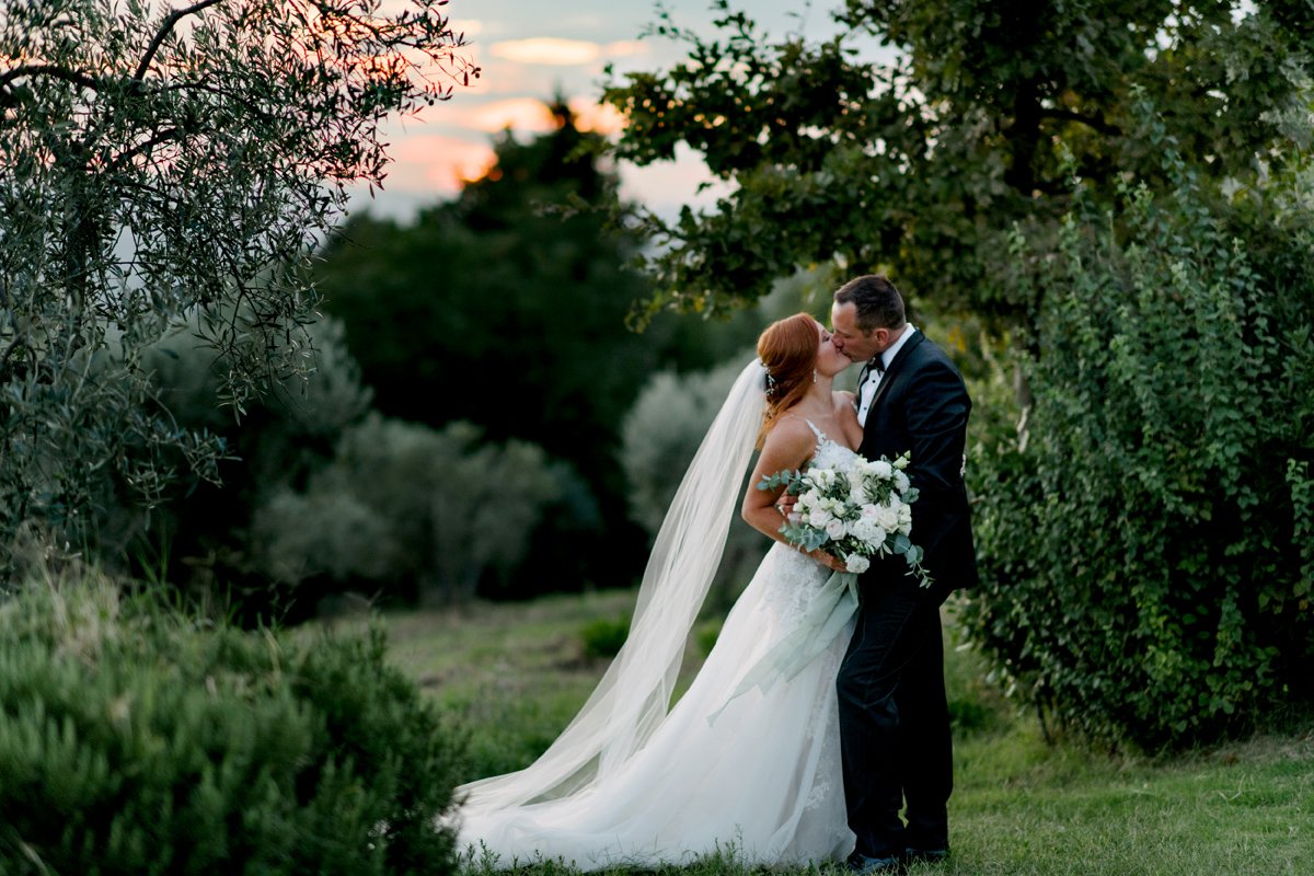 Romantische kus in het Toscaanse landschap bij Borgo Petrognano – een liefdevol moment tijdens een zorgvuldig geplande bruiloft in Italië.