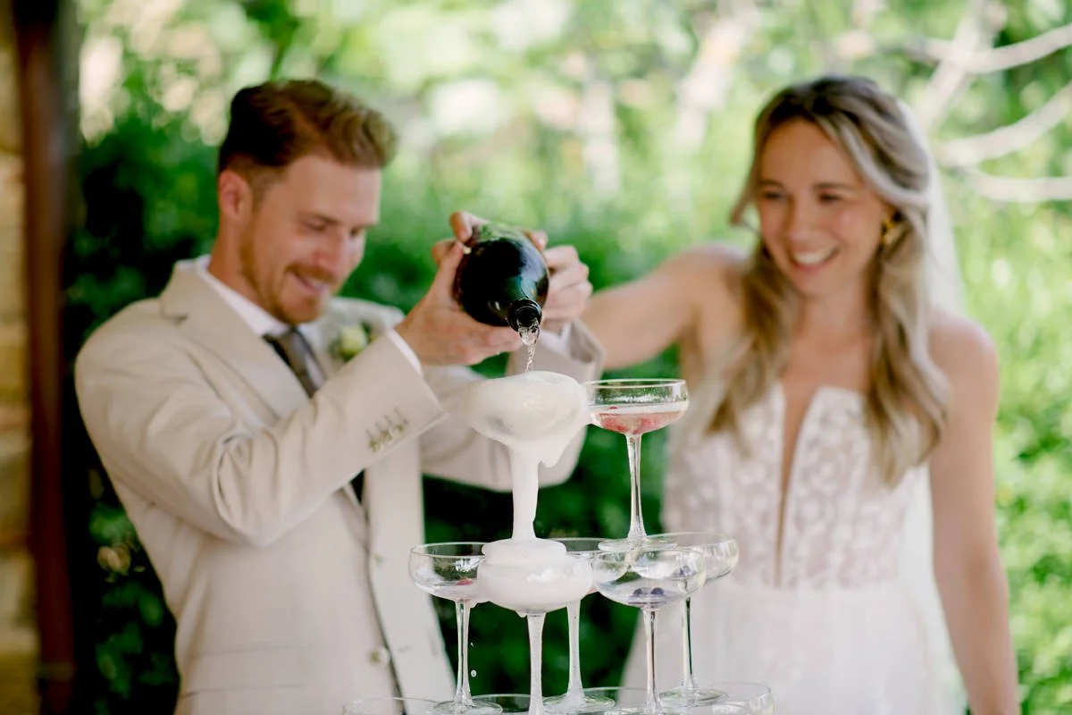 Bruidspaar schenkt champagne in een champagnetoren bij Borgo Petrognano – feestelijk moment tijdens een perfect gecoördineerde bruiloft in Toscane, begeleid door ceremoniemeester van FunkyBird Weddings.