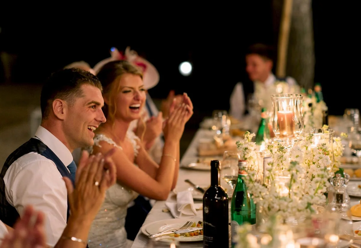 Bruidspaar lacht samen aan de dinertafel bij Conti di San Bonifacio – een spontaan en ontspannen moment tijdens een bruiloft in Italië, soepel begeleid door een ceremoniemeester.