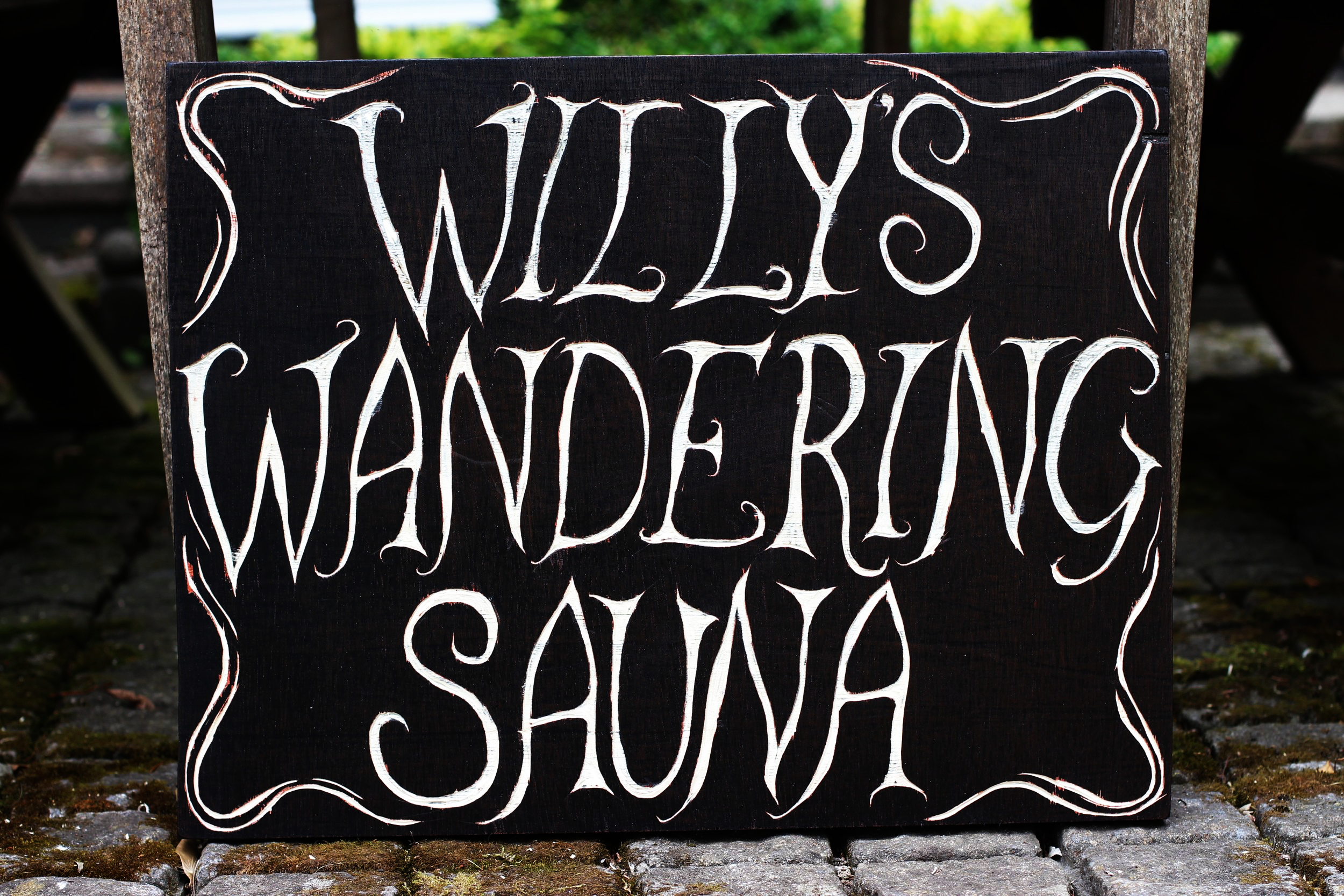 Black chalkboard sign with white handwritten text saying 'WILL'S WANDERINGS SALSA' on cobblestone ground.