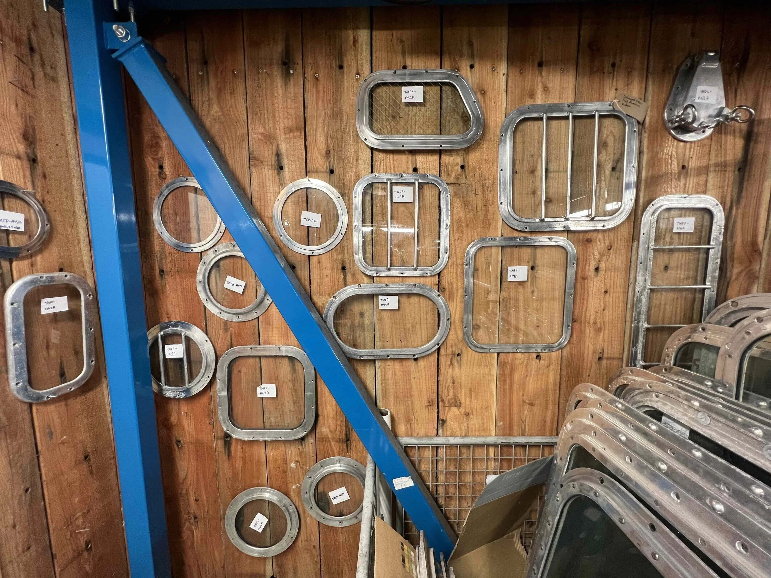 Metal window and hatch frames displayed on a wooden wall in a hardware store or workshop.