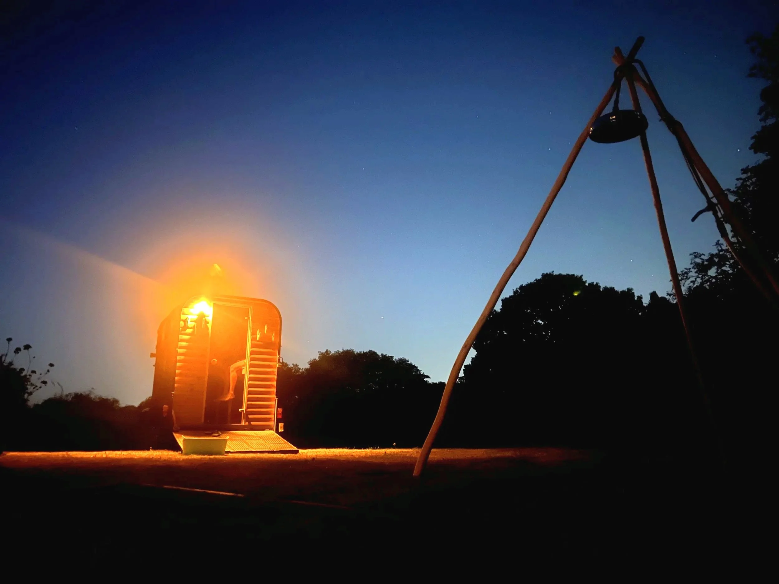 A playground at dusk with a swing set on the right and a small illuminated structure on the left, set against a darkening sky with a few visible stars.