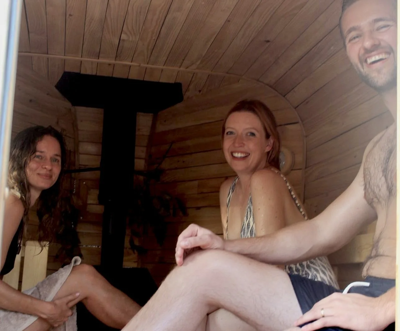 Four people sitting inside a wooden sauna, smiling and relaxing.