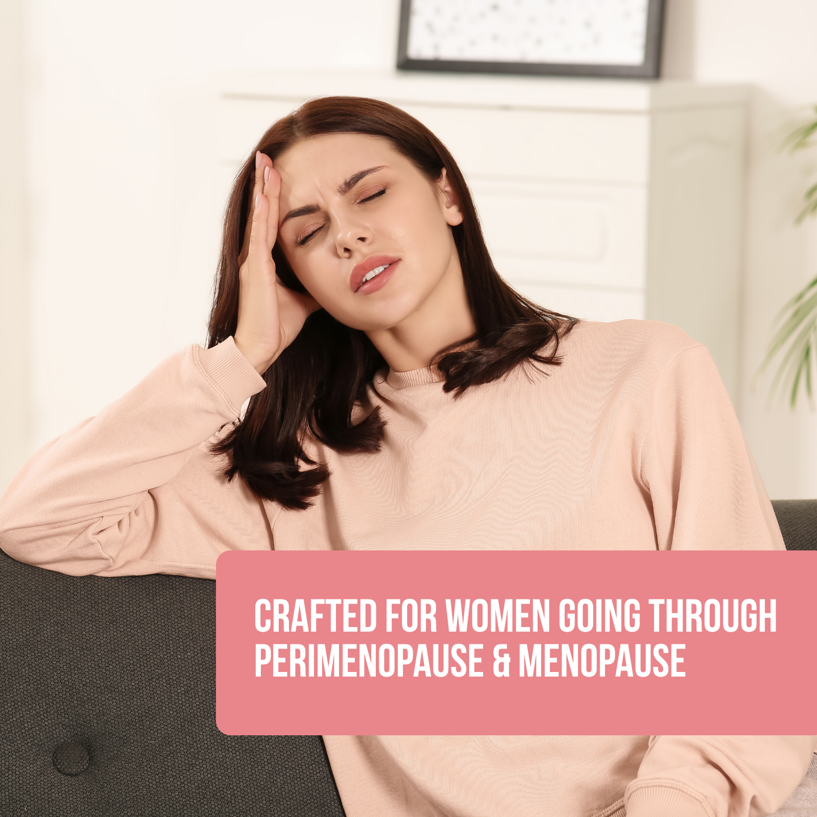 A woman sitting on a couch, holding her head with a pained expression, wearing a beige sweatshirt. Text overlay: Crafted for women going through perimenopause & menopause.