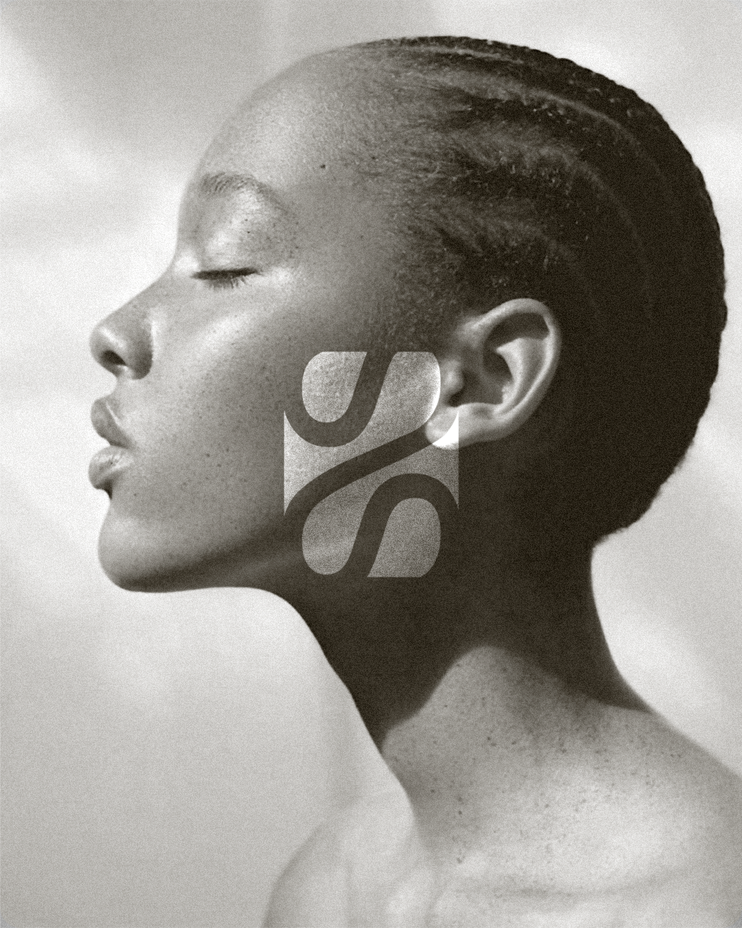 Black and white portrait of a woman with her eyes closed, featuring a close-up editorial-like profile of her face and neck, and the logo 'S' overlaid on her face.