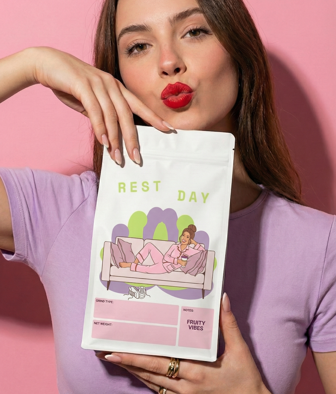 A woman with red hair, wearing a purple t-shirt, making a kiss face, holding a bag that says 'Rest Day' with an illustration of a woman lounging on a sofa against a pink background.