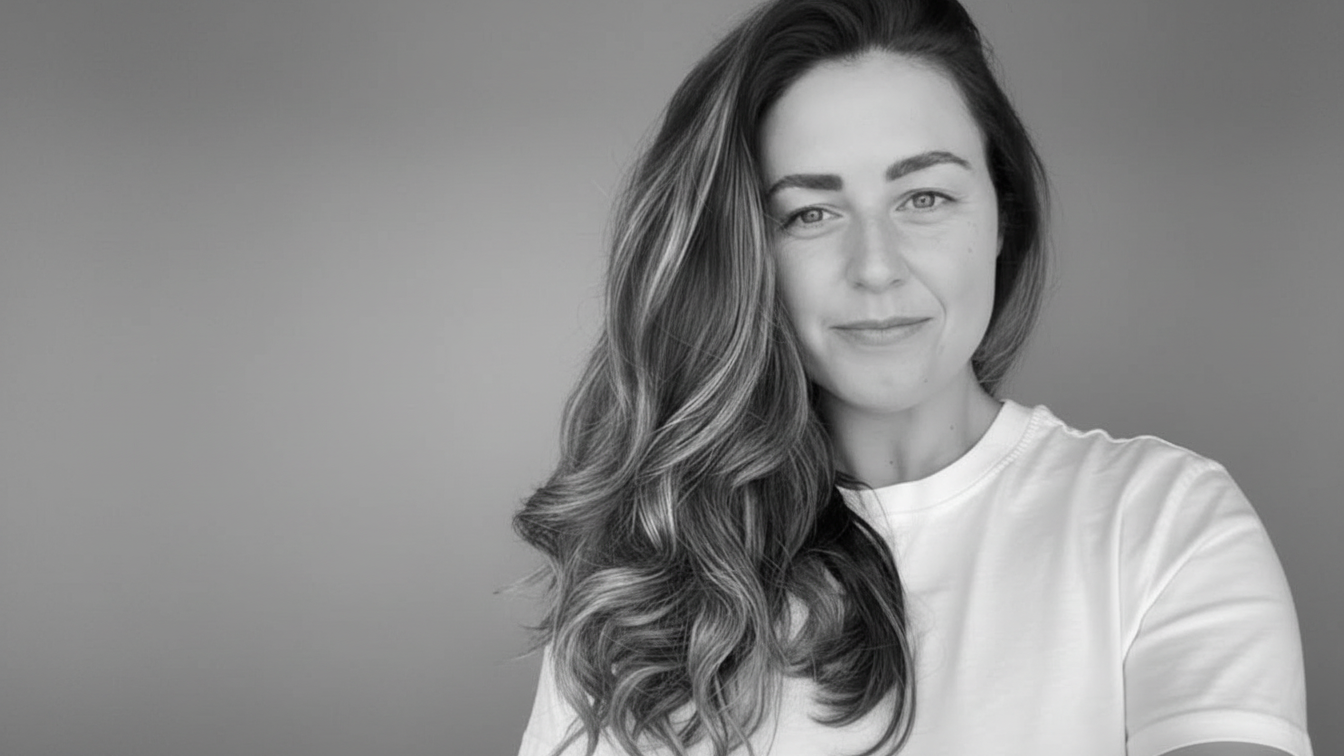 Black and white portrait of a woman with long wavy hair, wearing a t-shirt, looking at the camera with a slight smile.