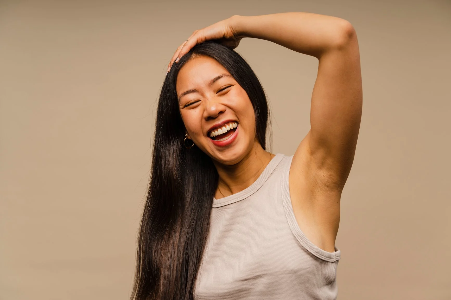 A woman with long, sleek, dark brown hair touching the top of her head with a big, happy smile on her face.