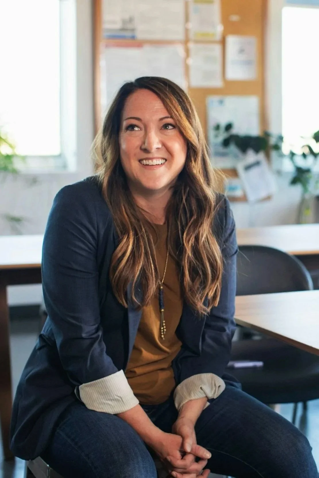 A brunette woman with beautiful, long, wavy hair that has blonde highlights and a warm, friendly smile.