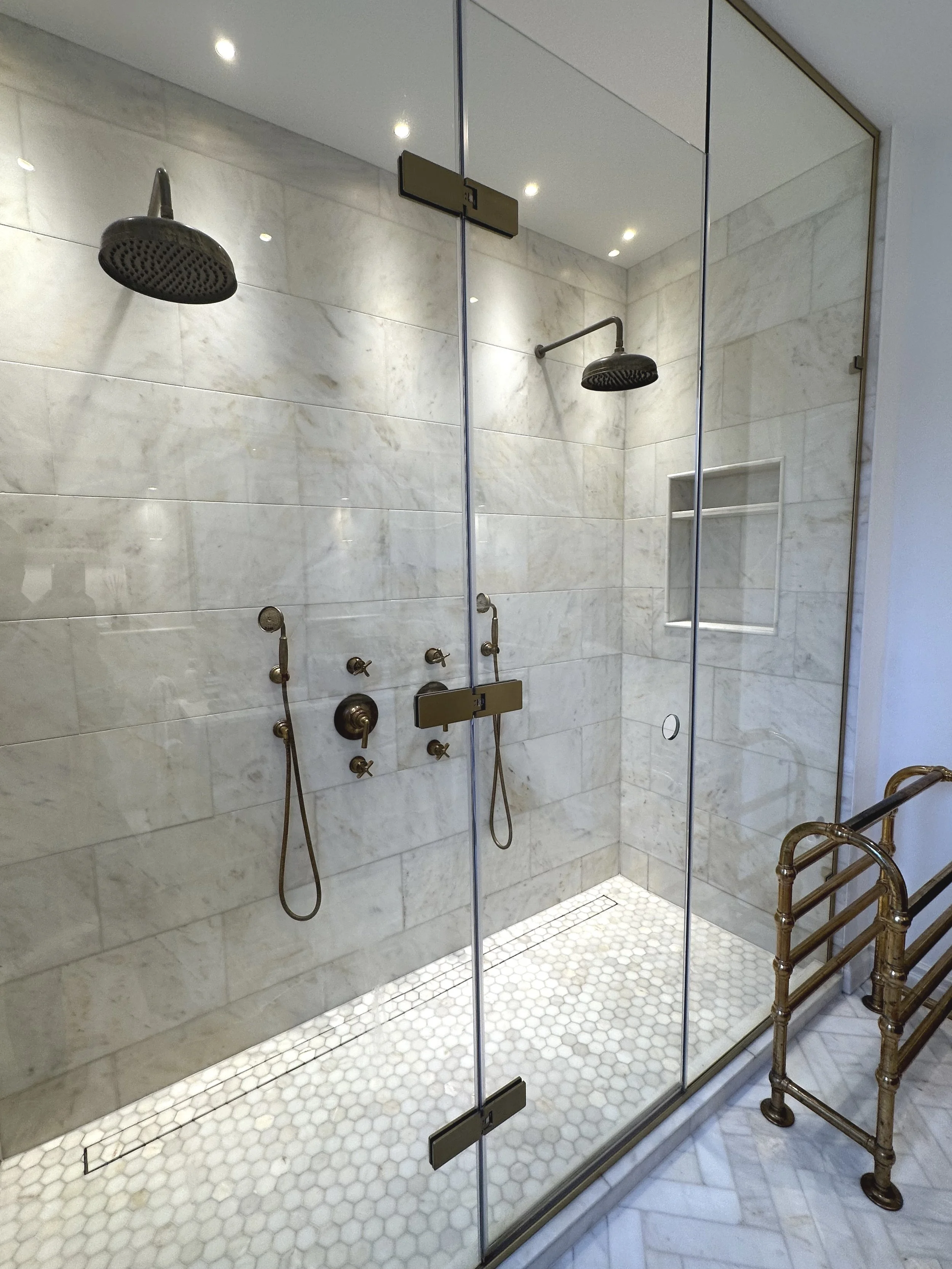 A modern walk-in shower with marble tile walls and two rain showerheads.