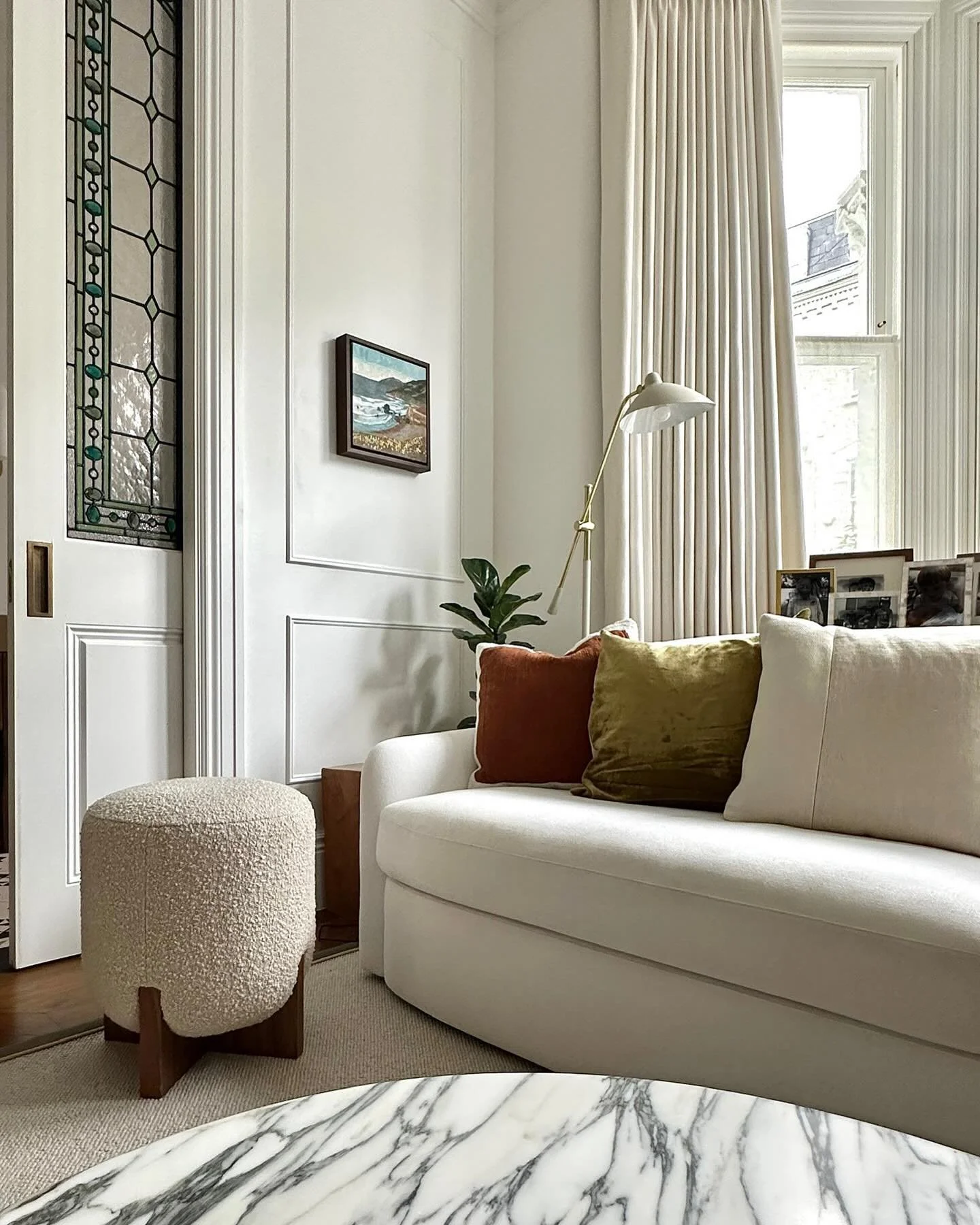 Reception room | Cozy, calm, and a little bit classic&mdash;just how I like it. I&rsquo;m loving how the soft textures, warm tones, and that curved @rh_restorationhardware sofa come together in this corner. The stained glass and marble bring in just 