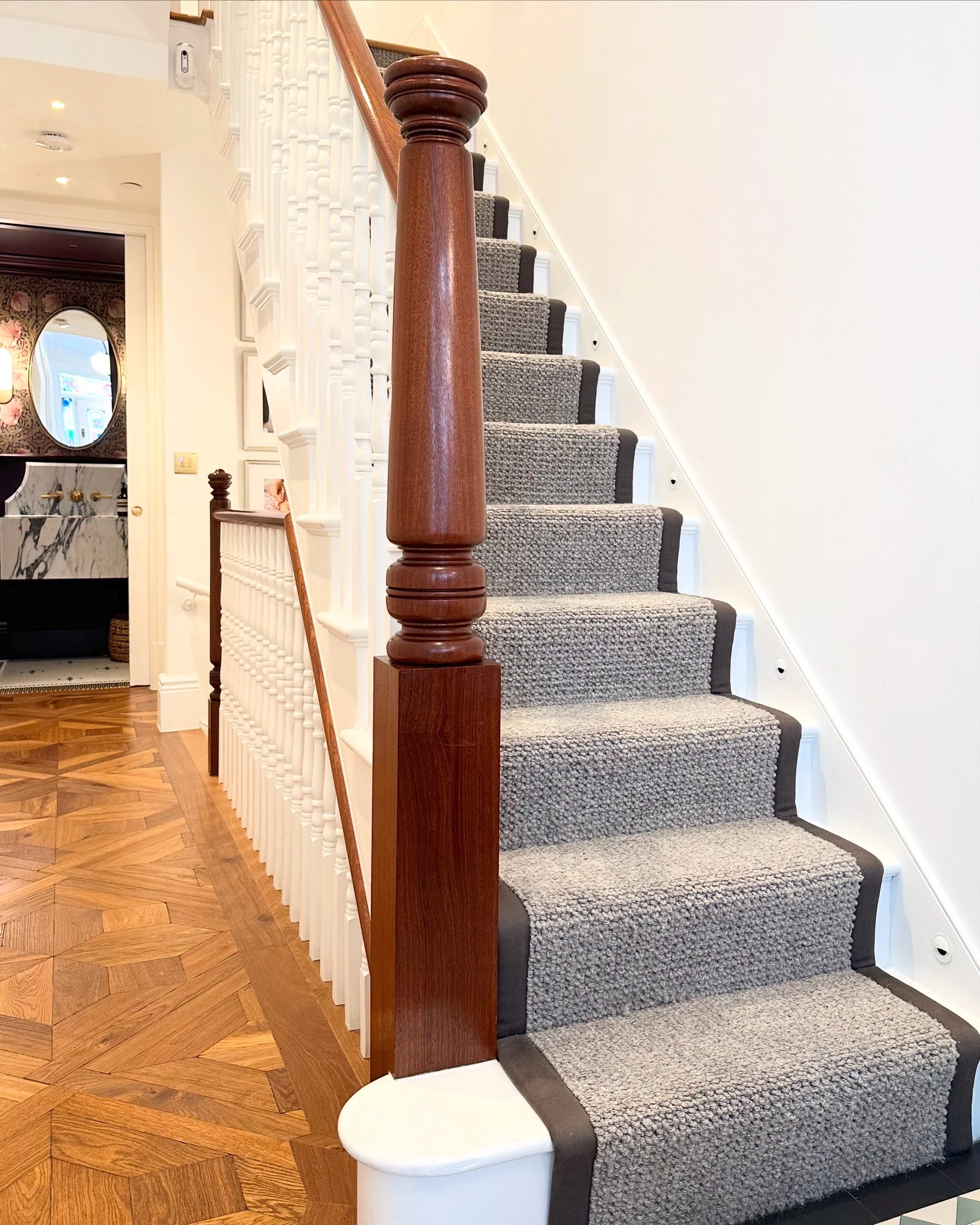 Interior view of a staircase with wooden banister, gray carpeted steps, and white walls in a modern home.