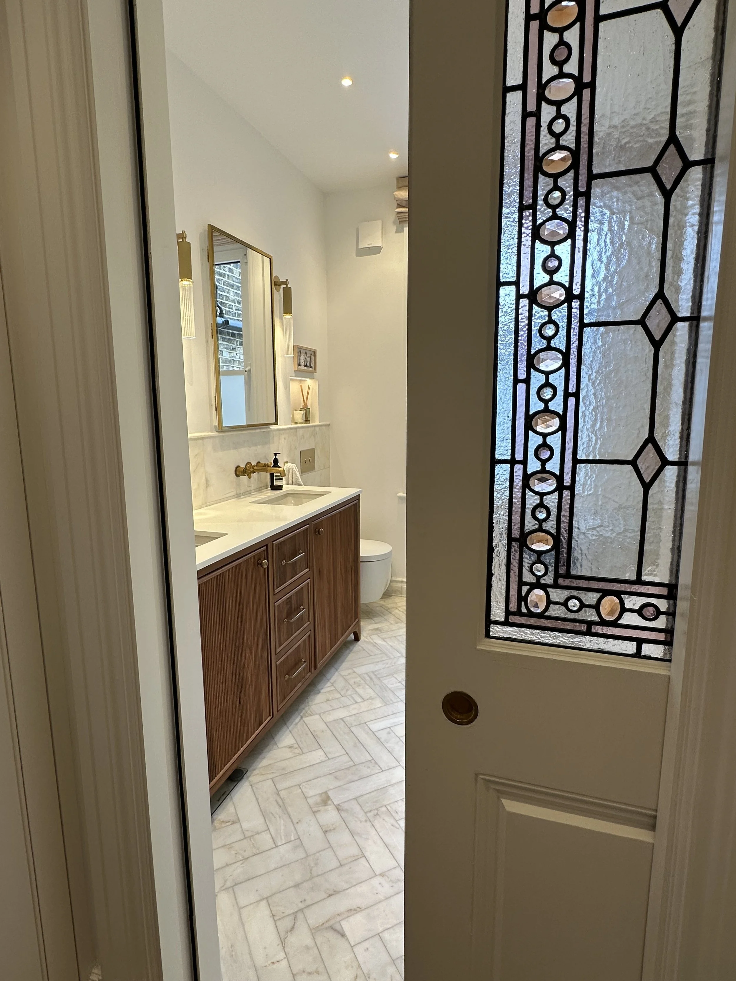 A view of a bathroom seen through an open door with a stained glass window on the side