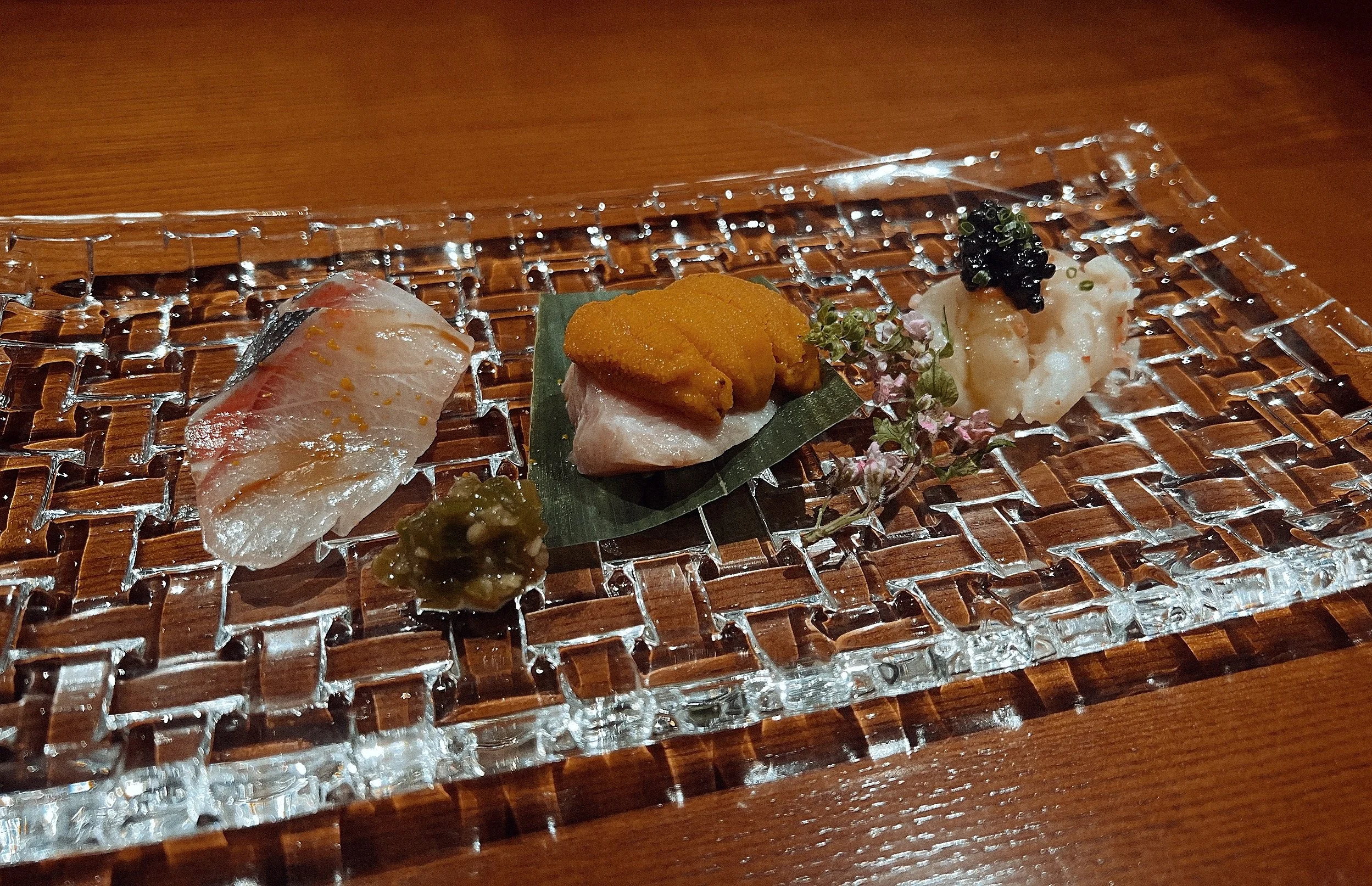 Assorted pieces of sushi arranged on a glass tray with a wooden surface underneath.