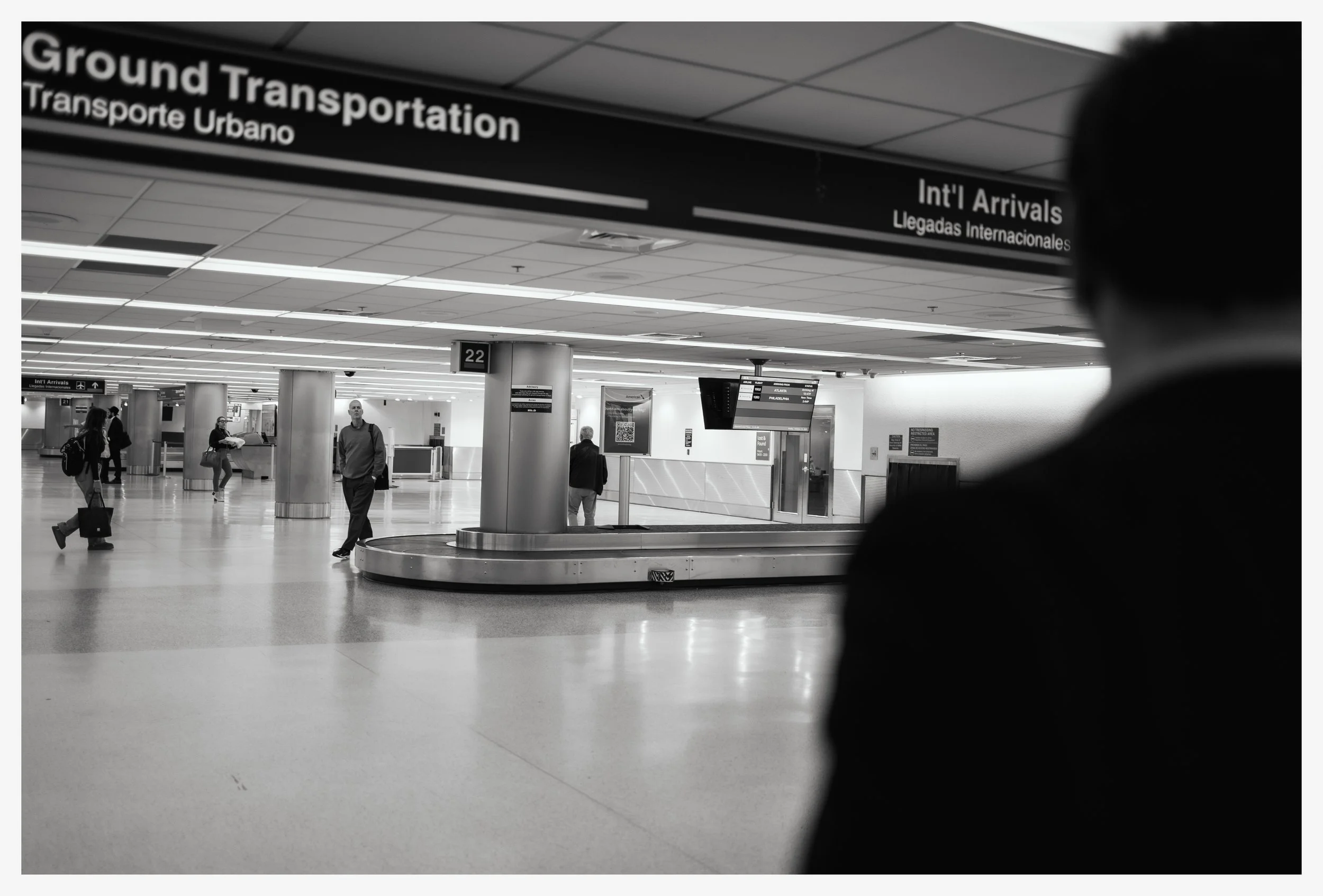 Interior of an airport terminal showing people walking near baggage claim area with an overhead sign indicating ground transportation and international arrivals.