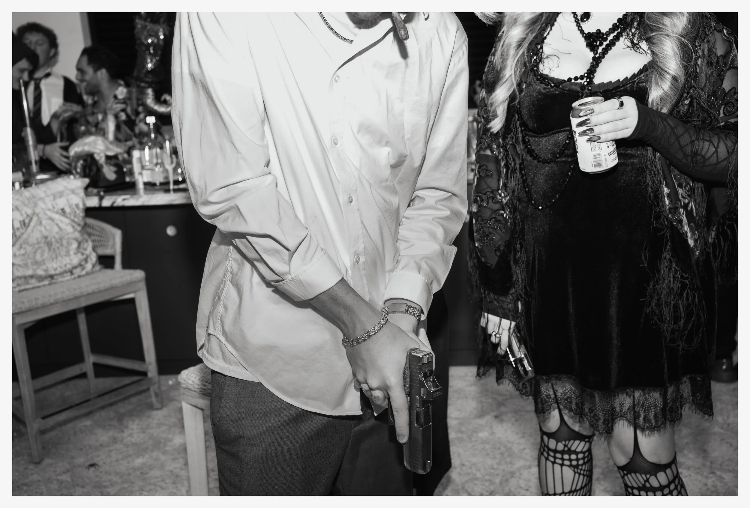 People at a party, one person holding a handgun in one hand with their finger inside the trigger guard.