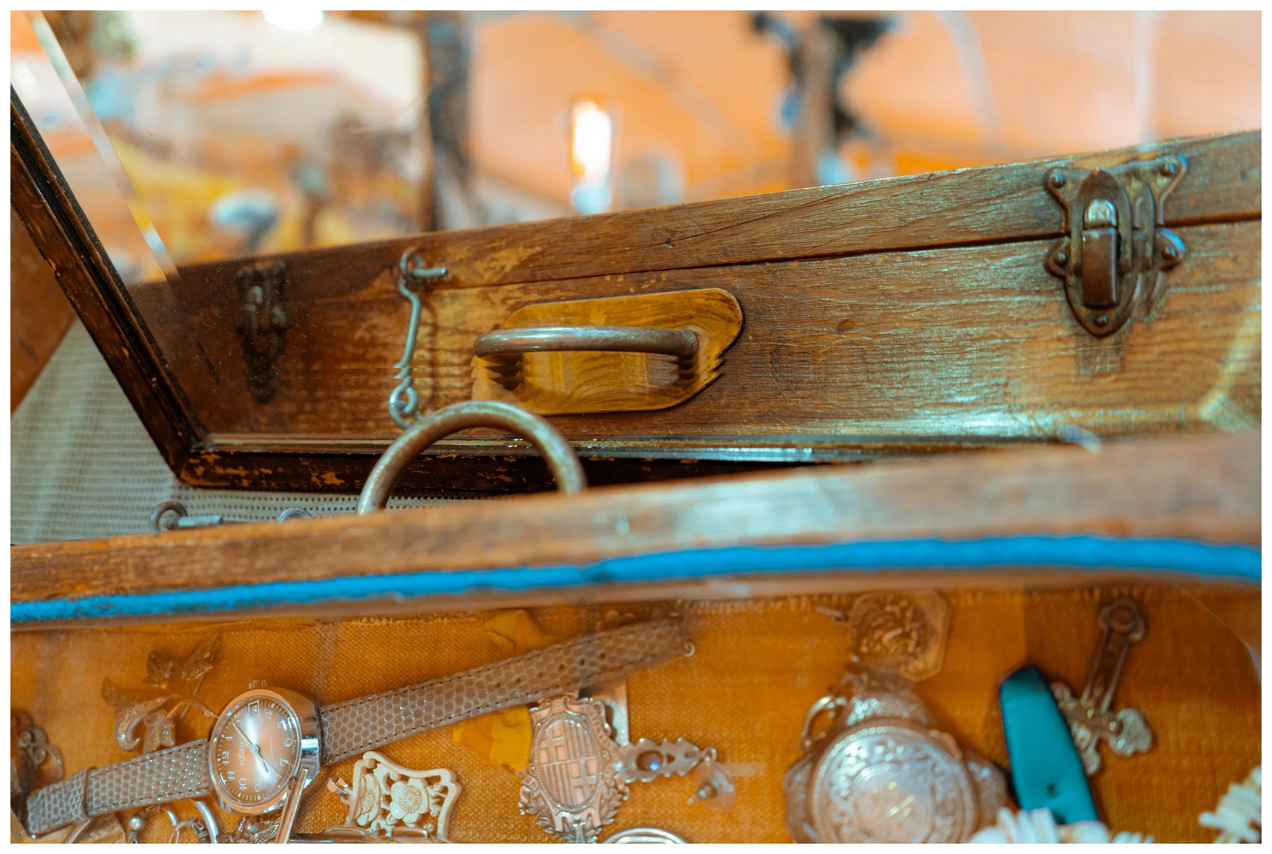 A wooden jewelry box with an open transparent glass lid, showing various vintage jewelry including watches, brooches, and chains inside.