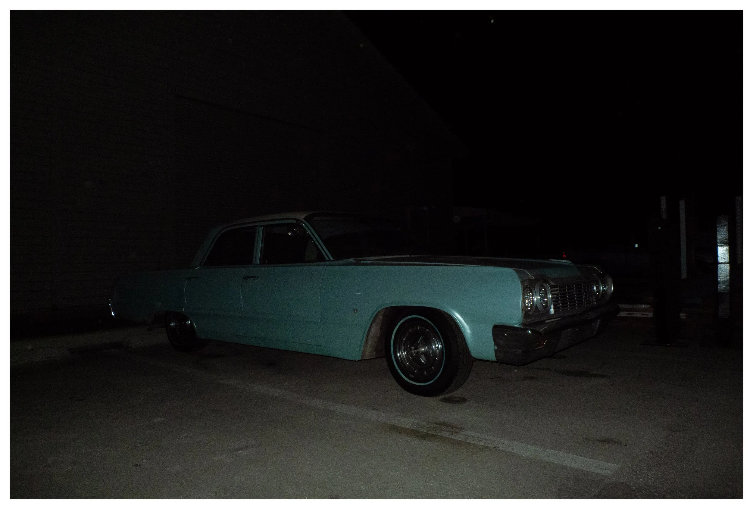 A vintage light blue car parked in a dark lot at night.