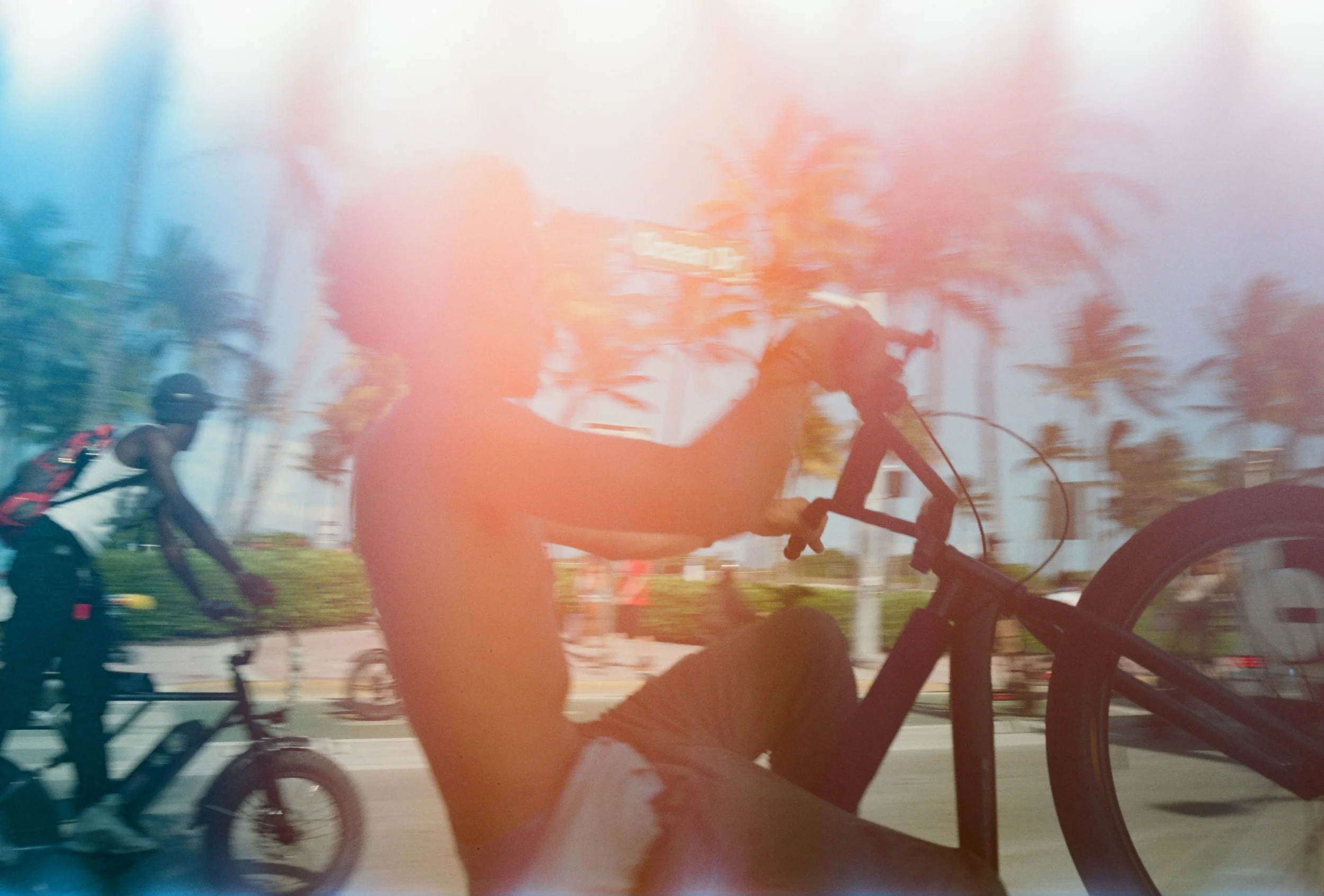 A blurry image of children riding bicycles on a street with trees and a building in the background.