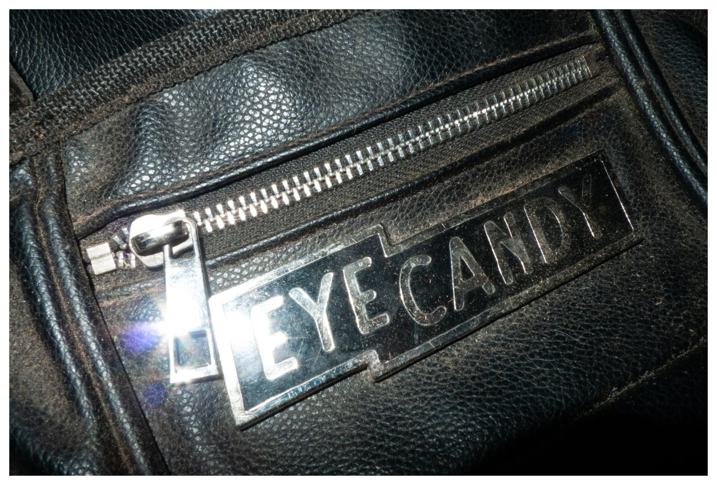 Close-up of a black leather jacket with a silver zipper and a metallic nameplate reading 'KEYE CANDY'.