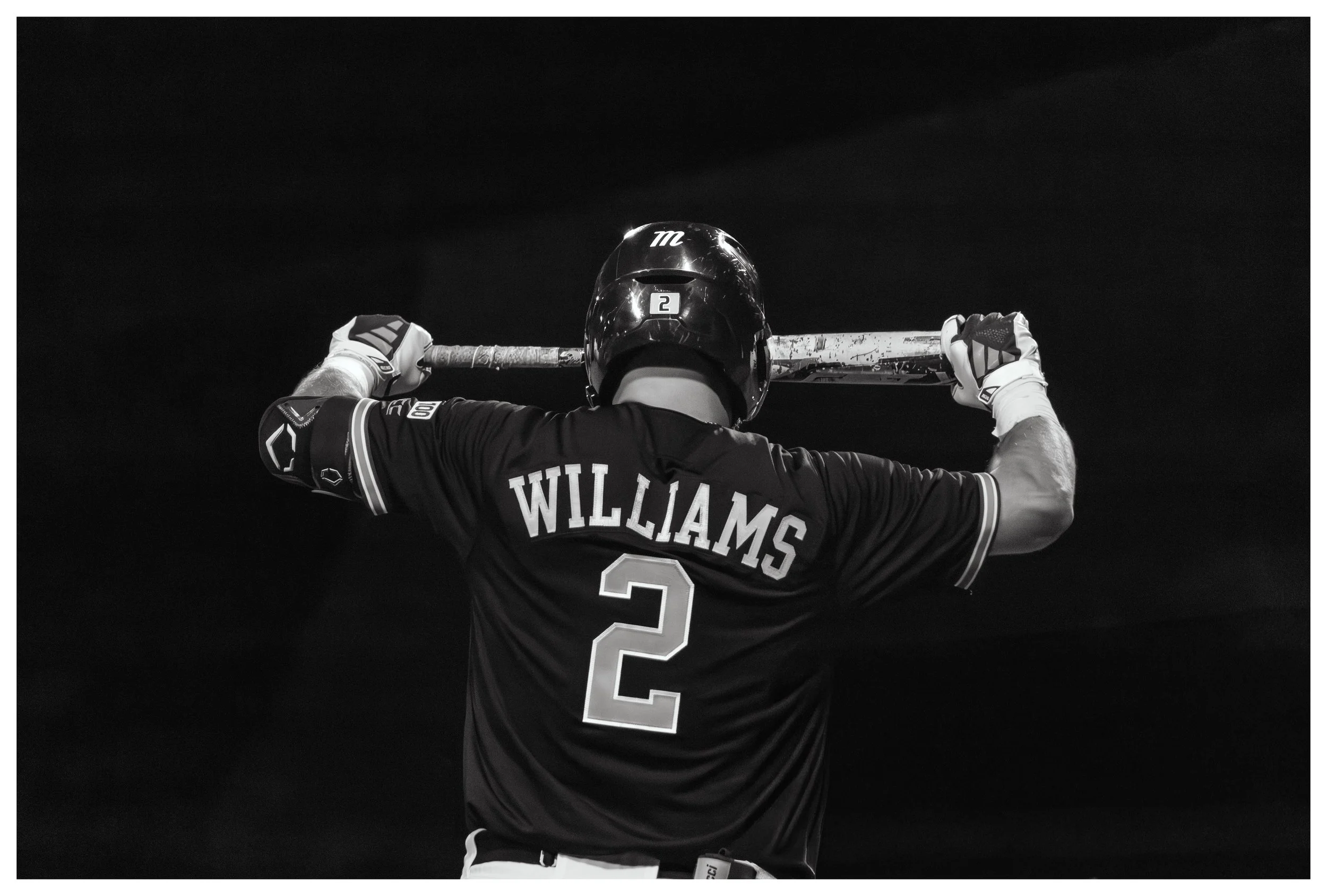 A baseball player in a black jersey with the name 'Williams' and the number '2' on the back, holding a bat across his shoulders, standing against a dark background.