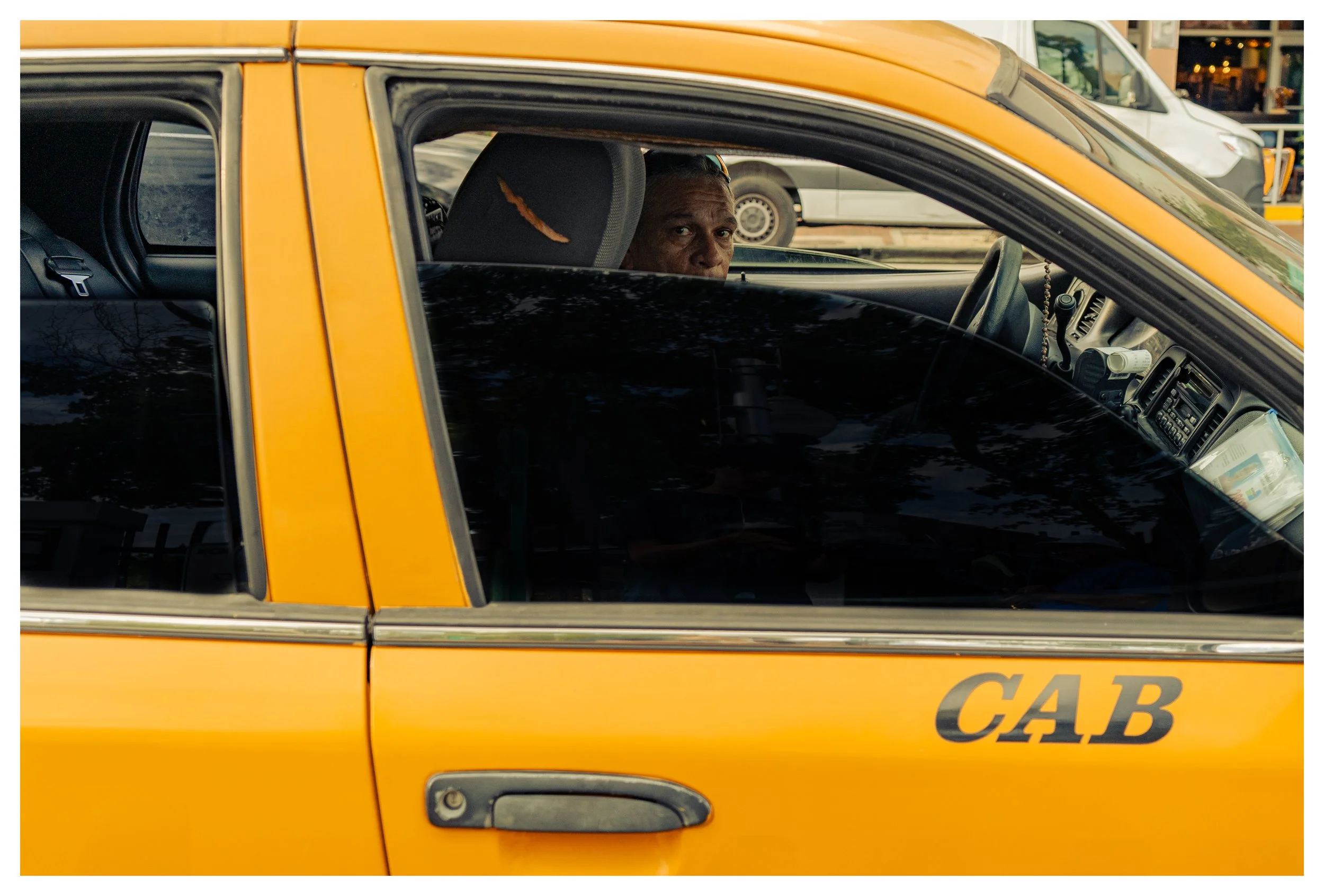 A man sitting in the driver's seat of a yellow cab, looking out the window.