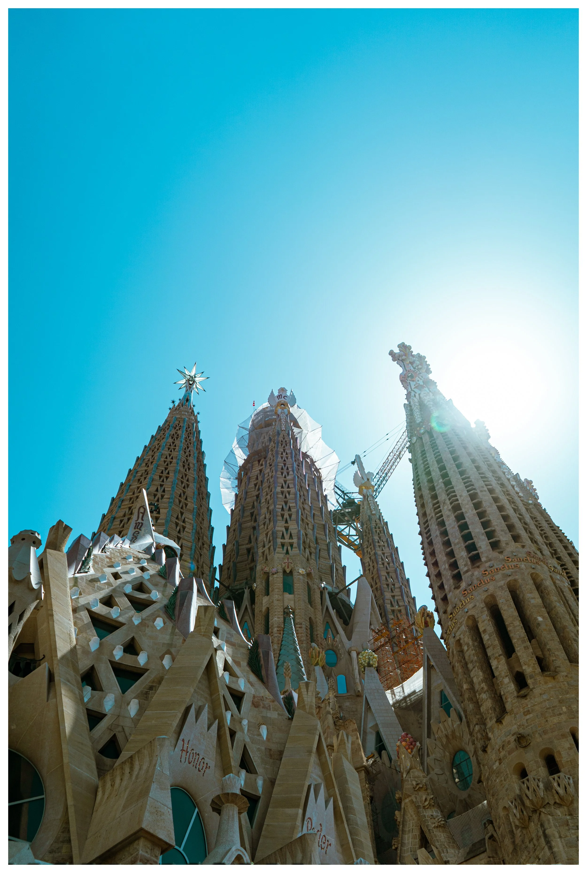 Sagrada Família basilica in Barcelona during daytime with a clear blue sky and sunlight shining behind the tower.