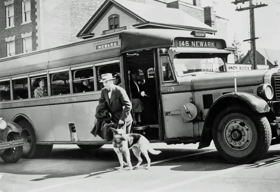 Black-and-white photo of a man and a German Shepherd stepping off a Newark bus marked route 146, c. 1930s.