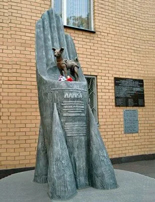 Monument of Laika, the first dog in space, standing atop a rocket-shaped pedestal, located in Moscow near a scientific institute building.