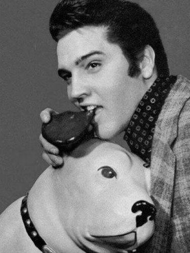 Elvis Presley playfully poses with a gramophone prop near a large model of Nipper the dog, referencing the iconic His Master’s Voice logo in a promotional photo.