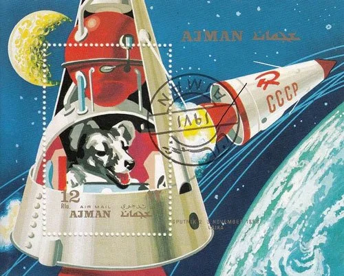 A colorful Ajman postage stamp showing Laika, the Soviet space dog, inside the Sputnik 2 capsule against a cosmic background with Earth and the Moon