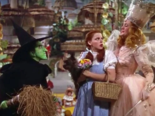 Dorothy clutches Toto and a bouquet while standing between Glinda and the Wicked Witch of the West in a tense, colourful scene from The Wizard of Oz (1939).