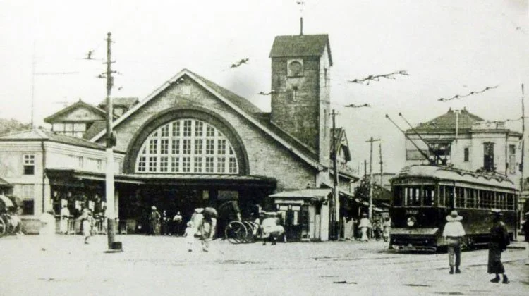 Early 20th-century view of Shibuya Station with pedestrians, streetcars, and surrounding buildings in Tokyo.