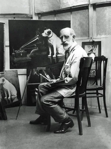 Artist Francis Barraud sits with a palette and brushes in his studio, beside his famous painting of Nipper the dog listening to a gramophone in His Master’s Voice.