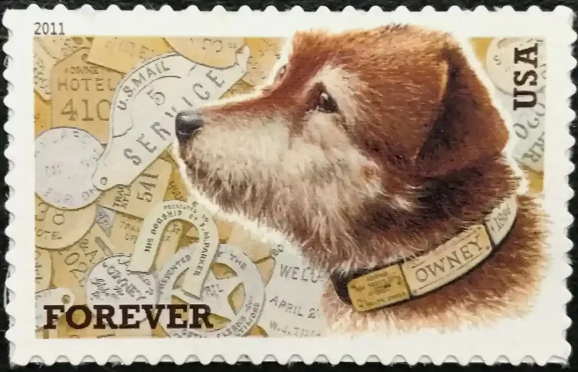 A 2011 U.S. Forever postage stamp featuring a profile of a scruffy brown dog named Owney wearing a brass collar. The background is a collage of vintage mail tags with a perforated white border.