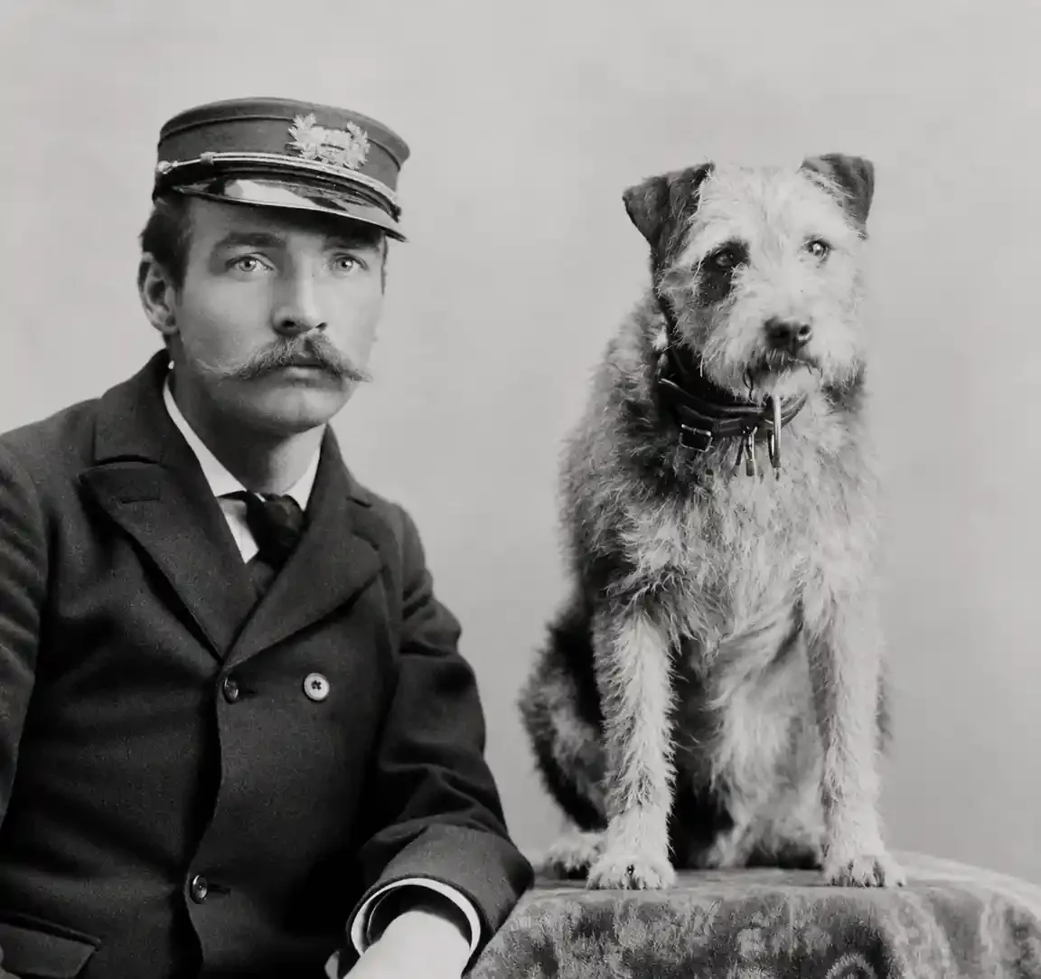 A mustached mail clerk in a peaked uniform cap sits beside a wire-haired terrier