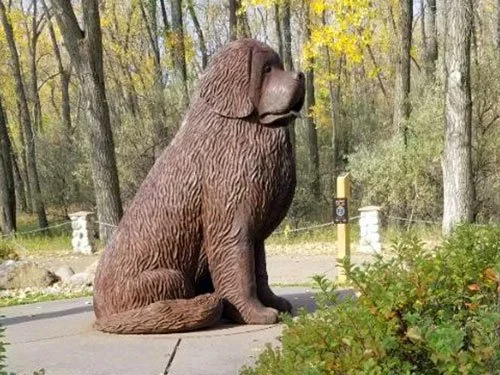 Large statue of Seaman, the Newfoundland dog who accompanied the Lewis and Clark Expedition, seated beside a forest path.