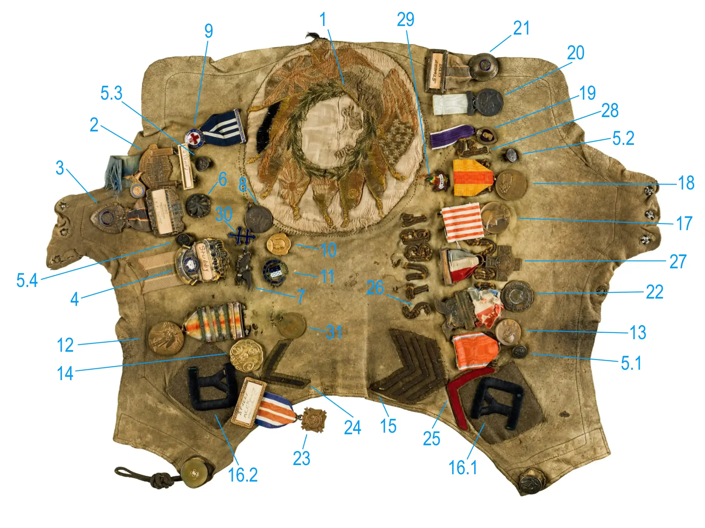 Worn chamoise dog blanket laid flat, covered with WWI medals, badges, stripes, and pins, each item numbered and labeled for identification.