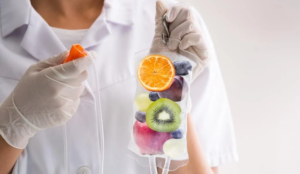 Person in medical attire holding a clear bag with various sliced fruits, including orange, kiwi, blueberry, and grape.