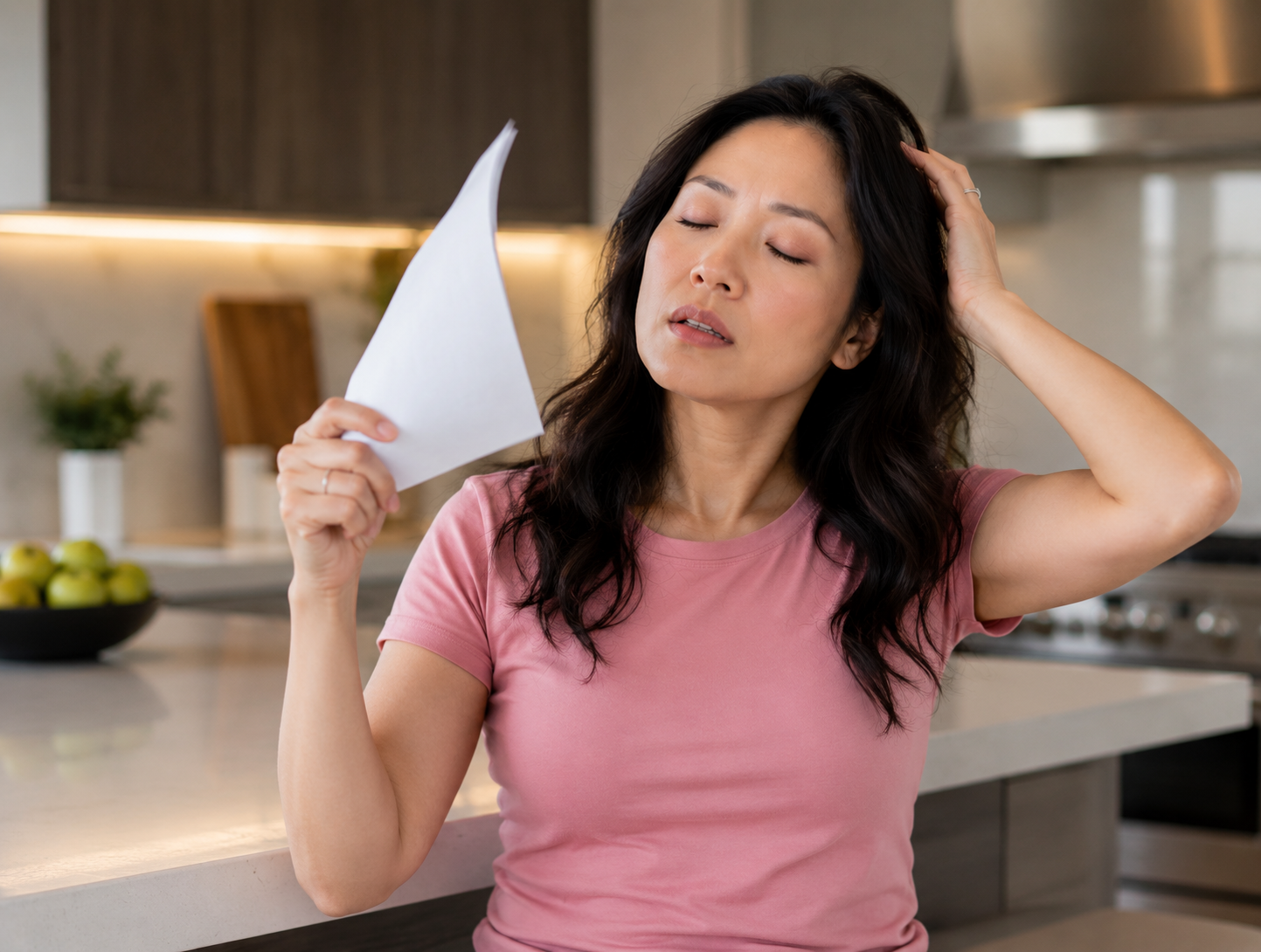 Asian woman experiencing hot flash symptoms after breast cancer treatment in a modern kitchen