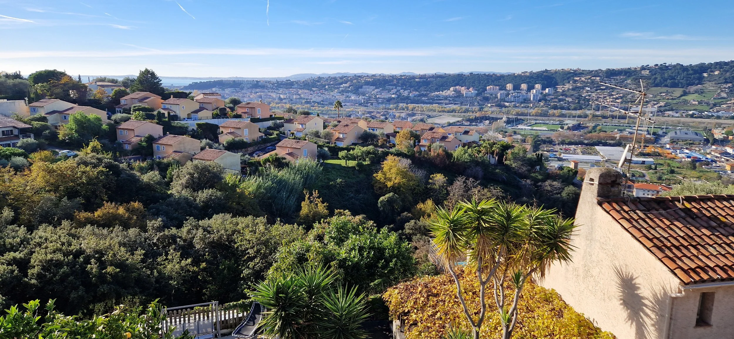 Kattava näköala kaupunkimaisemasta, vuoristoisista maastoista ja taivaasta, näkyvissä on omakotitalojen pihoja, puita ja antenneja.