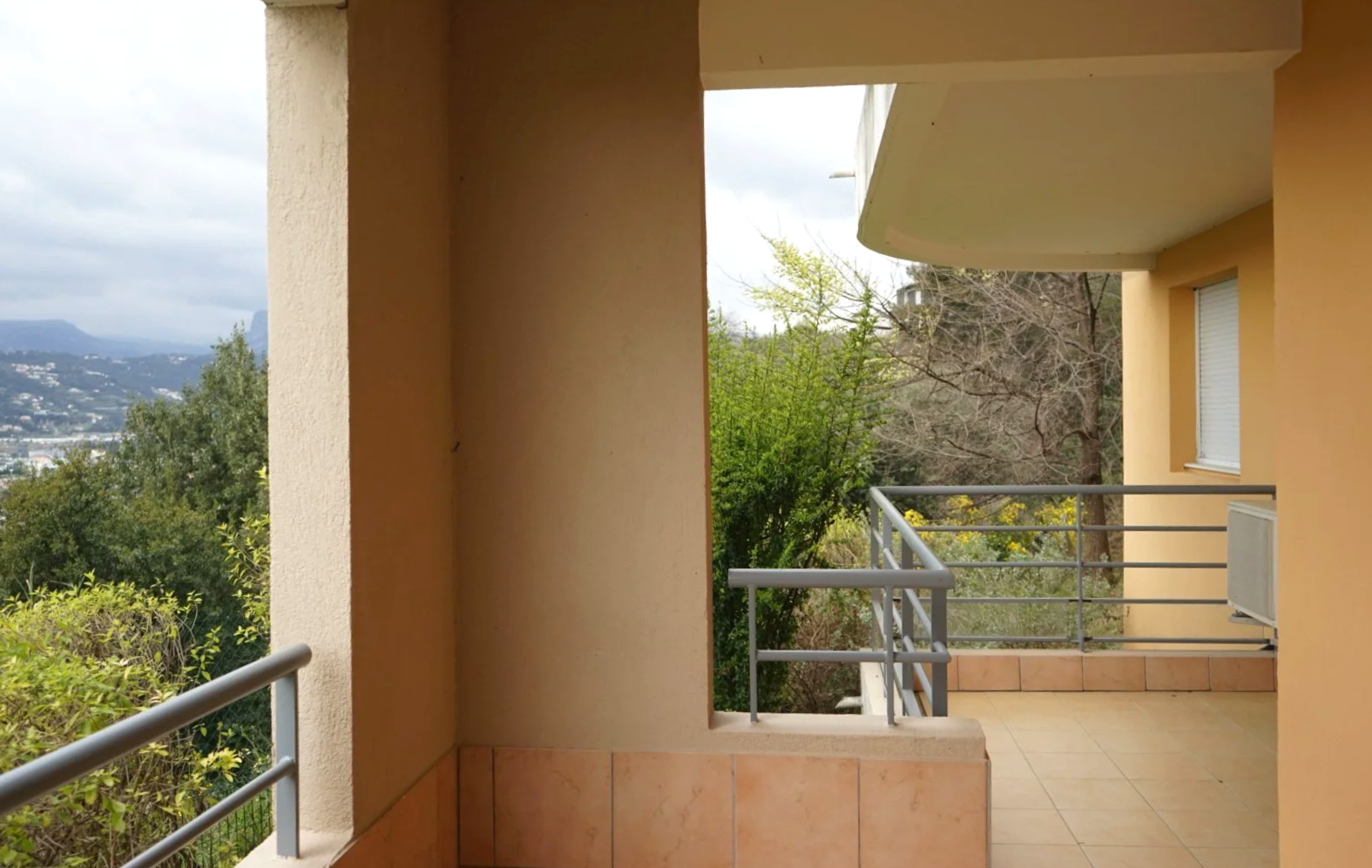 Kuisti tai parvekkeella, näkymä puutarhaan ja maisemaan, pussipuut ja pilvinen taivas.