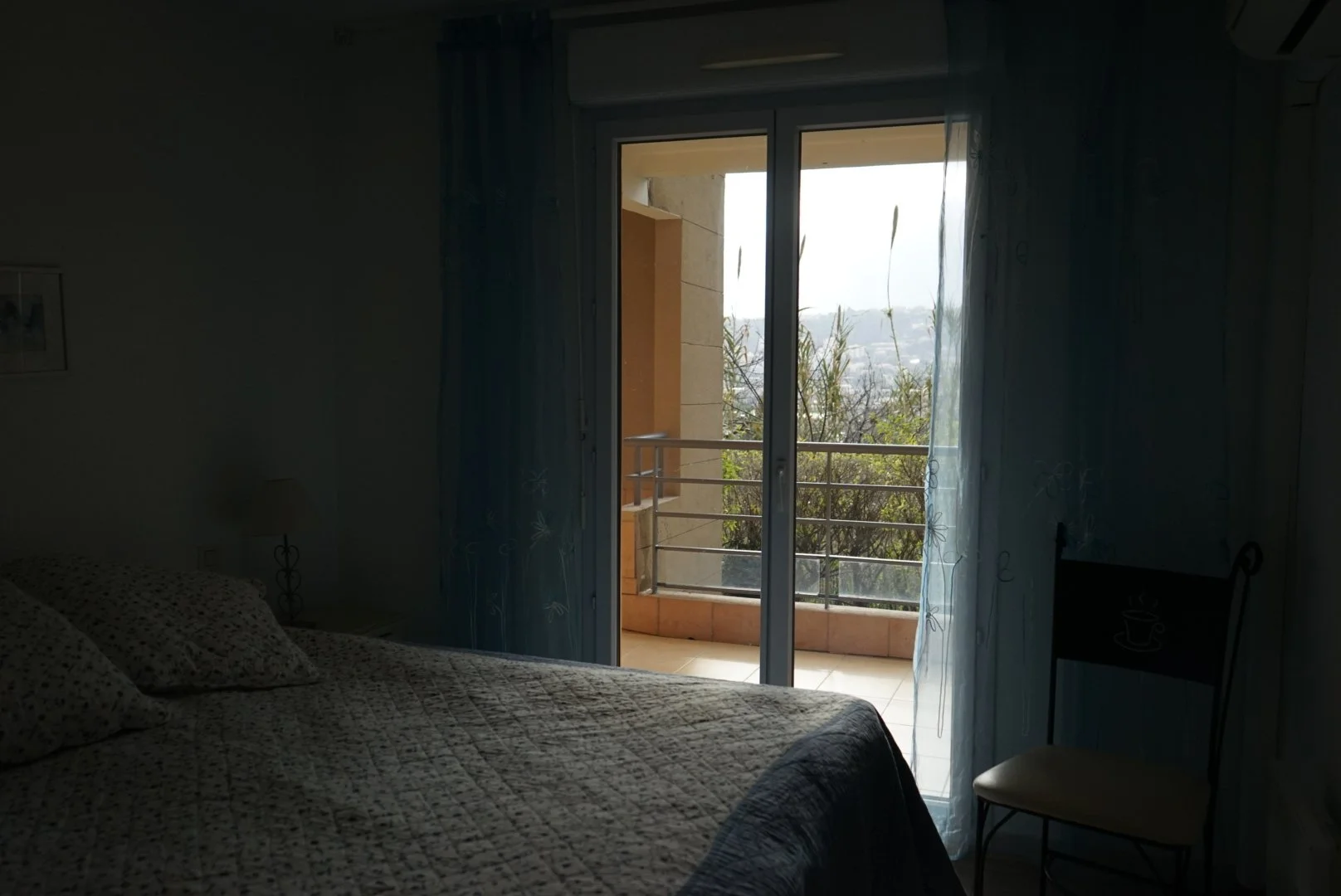 Hämäräkuva hotellihuoneesta, eteinen ja vuode näkyvissä, parveke ja maisema ulkoa näkyvissä.