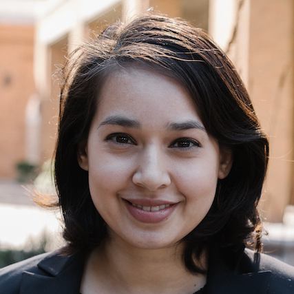 Portrait of a young woman with dark hair smiling outside during daytime.
