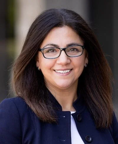 A smiling woman with shoulder-length dark hair, wearing glasses and a navy blazer.