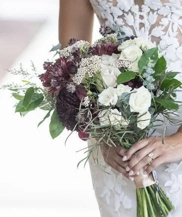 A bridal bouquet completed with purples, greenery, and white flowers arranged by Laura at Design & Gather.