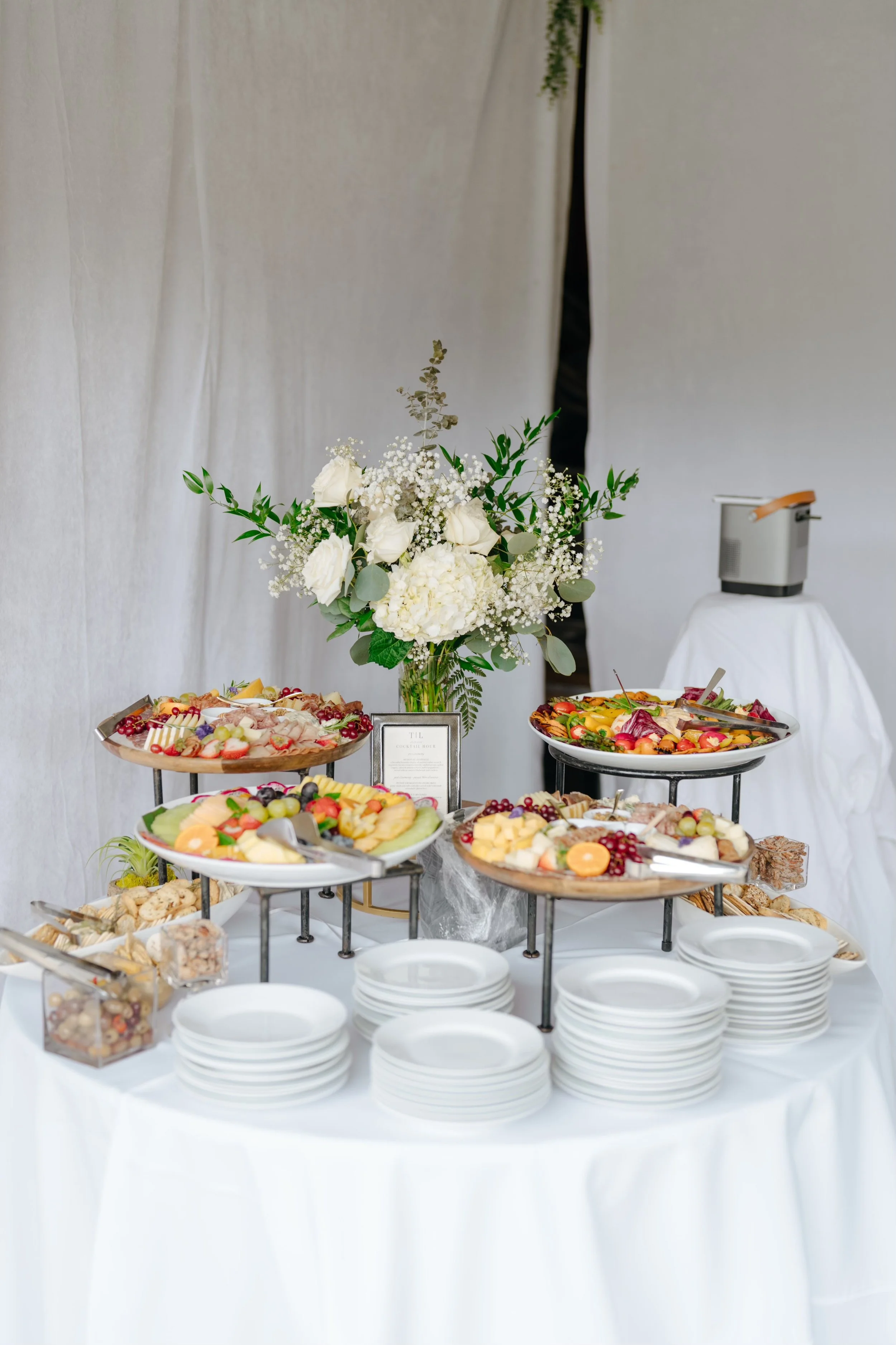 Buffet table with a flower arrangement and various fruit and appetizer platters at a catered event.