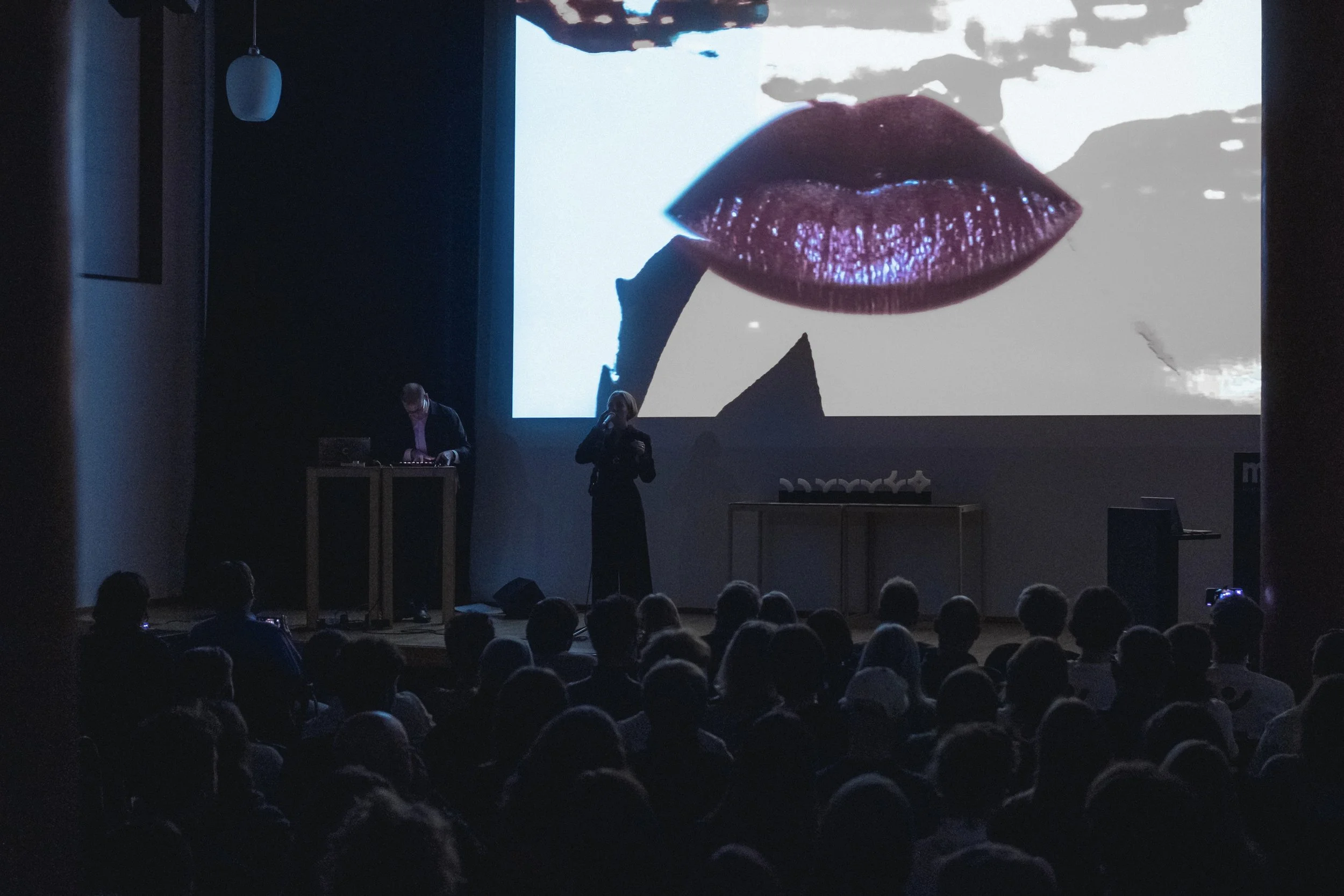 Hannah Otto und Ahmetcan Gökçeer live auf der Bühne vor vollem Publikum mit Musikvideo-Projektion im Hintergrund bei der Preisverleihung des Kölner Designpreis 2024 im Museum für angewandte Kunst Köln