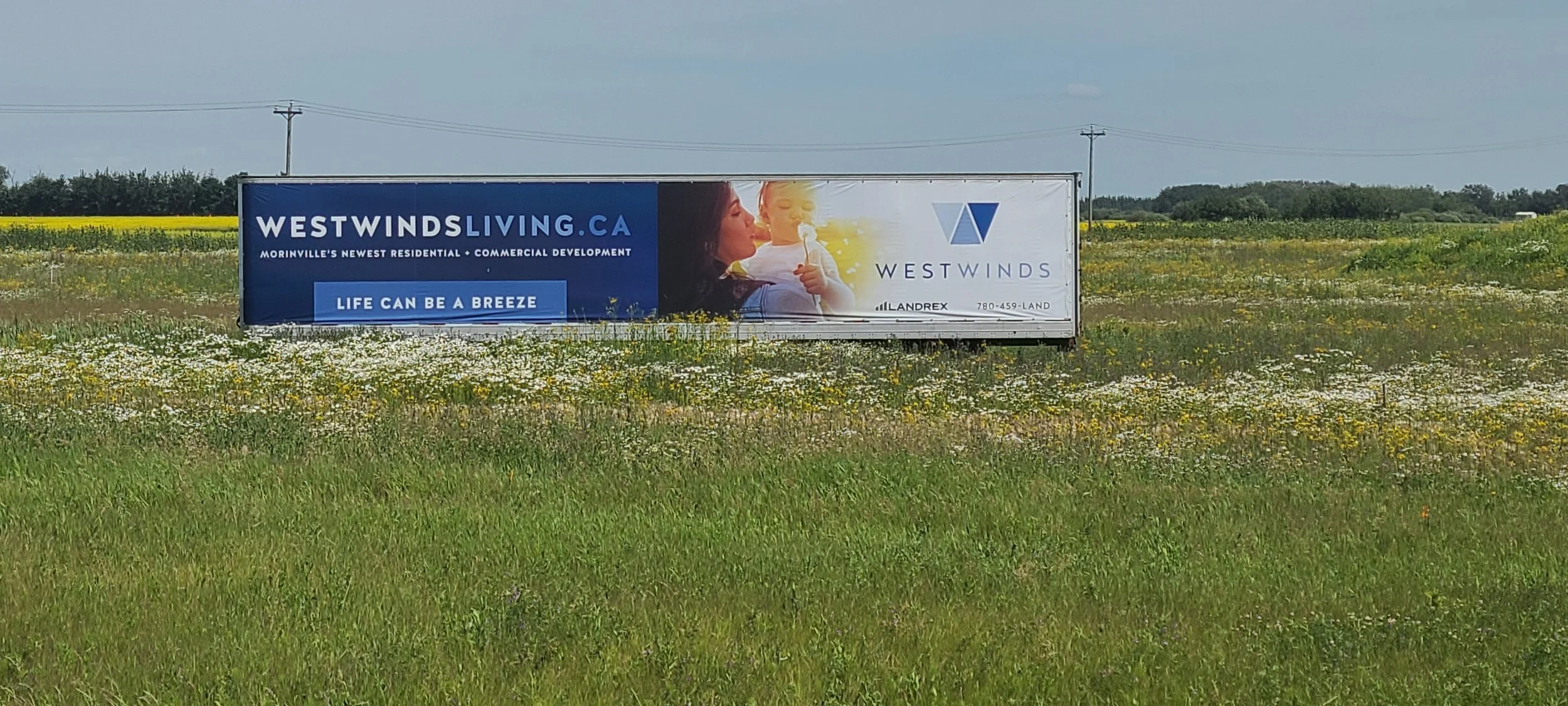 Large outdoor billboard advertising Westwinds residential and commercial development in Morinville, Alberta, Canada, with a woman and a child in the background.
