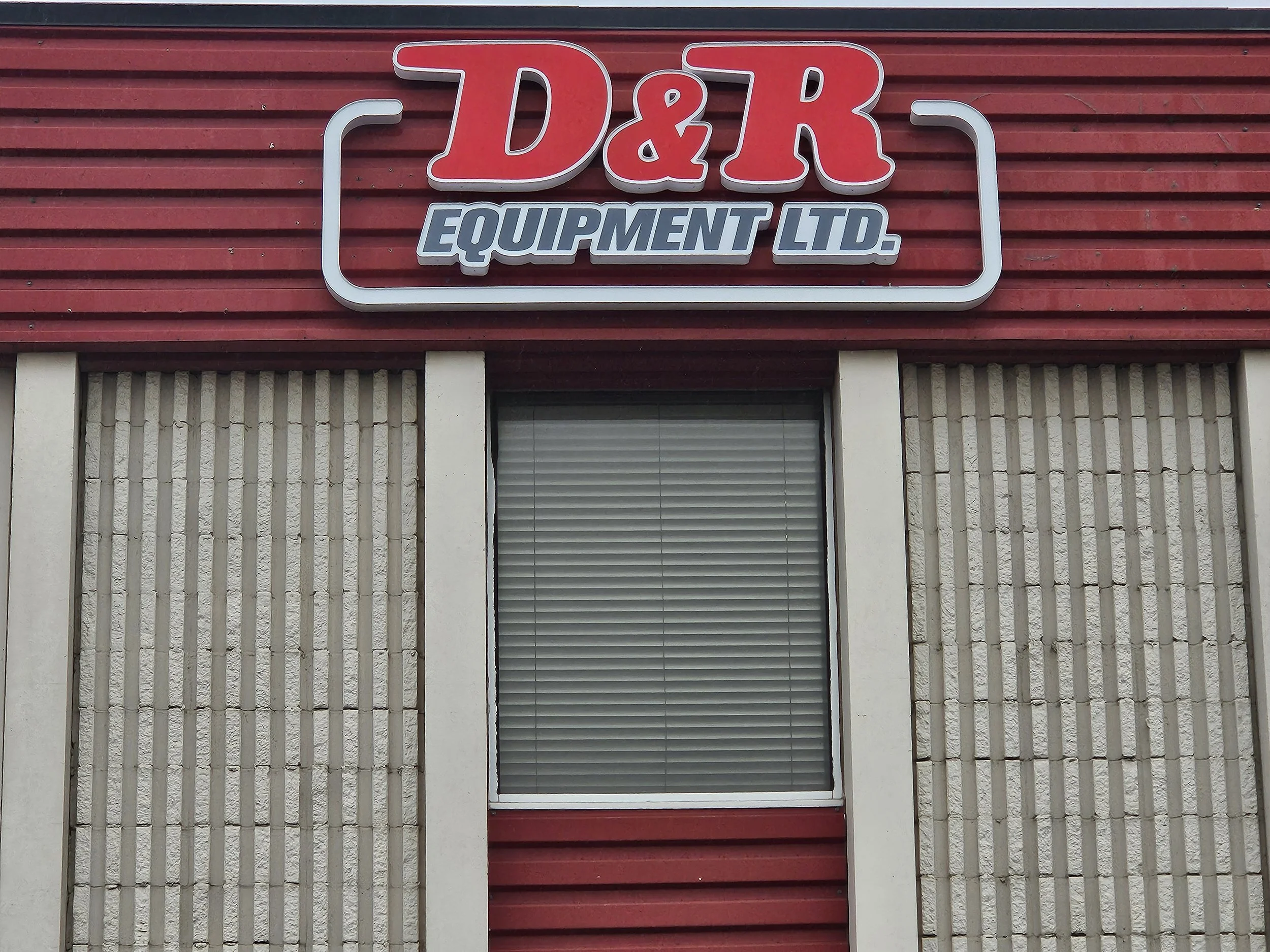 Sign for D&R Equipment Ltd. above a window on a red building with beige concrete blocks.